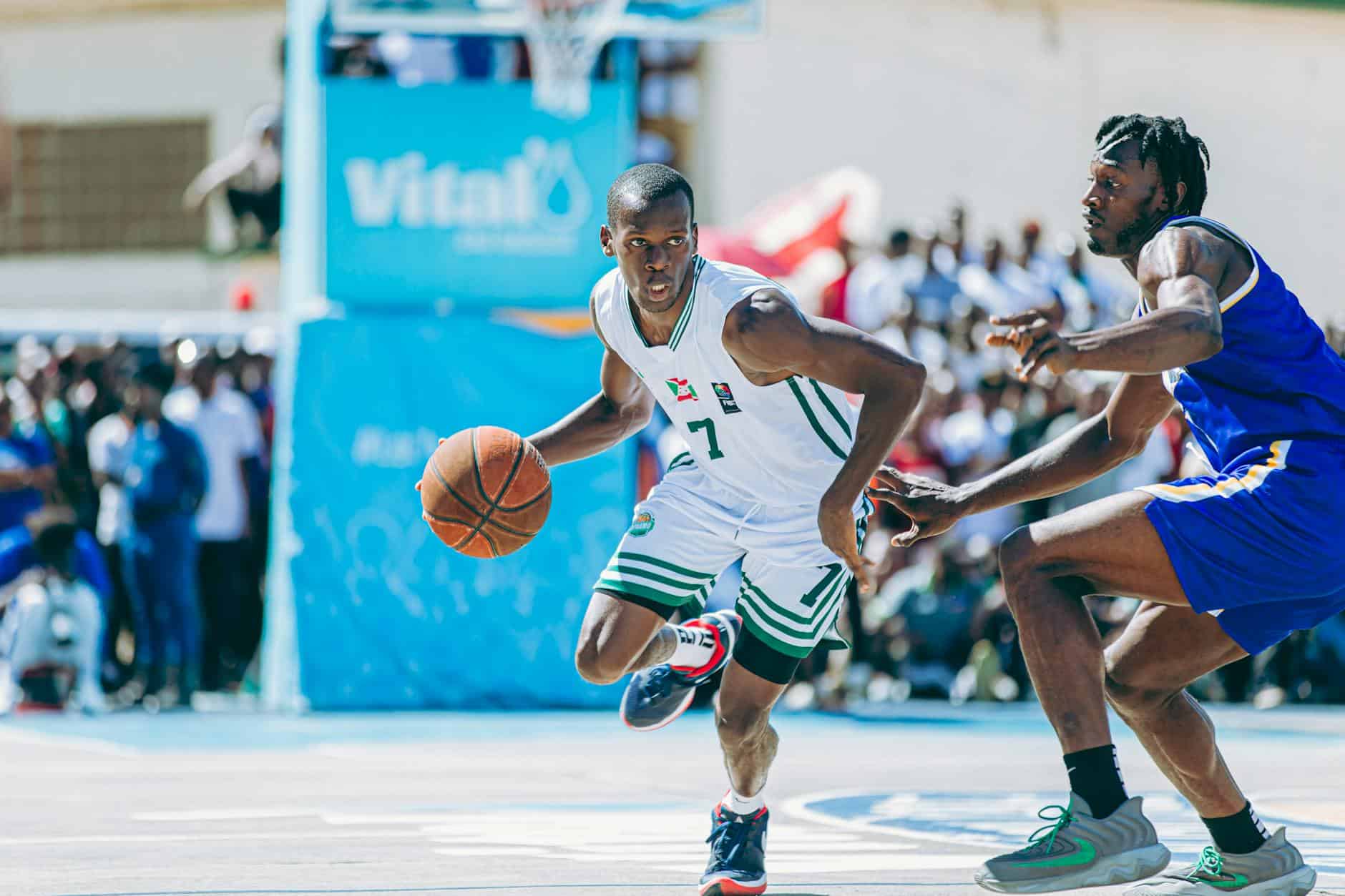 Basketball player in white jersey dribbling the ball while being defended in a game.
