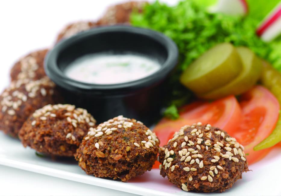 Crispy falafel balls topped with sesame seeds served with fresh vegetables and creamy tahini sauce, perfect for a delicious Middle Eastern appetizer or meal.